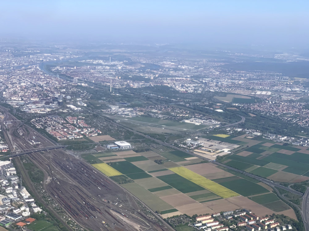 Luftaufnahme von Mannheim mit dem Flughafen, städtischen Gebieten und Feldern im Vordergrund.