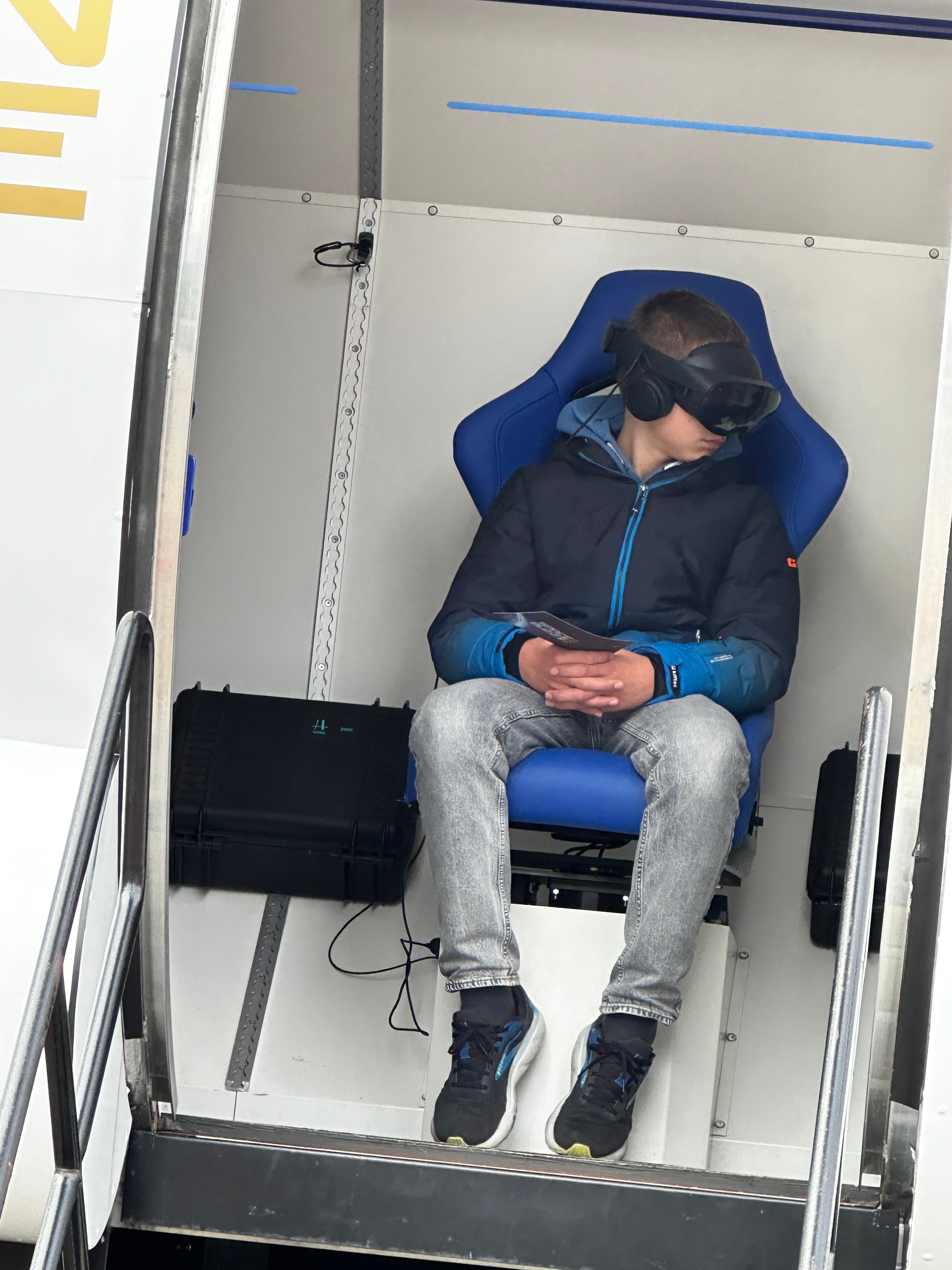 Ein Junge sitzt in einem blauen Stuhl mit VR-Brille und Kopfhörern, während er in einem geschlossenen Raum sitzt.