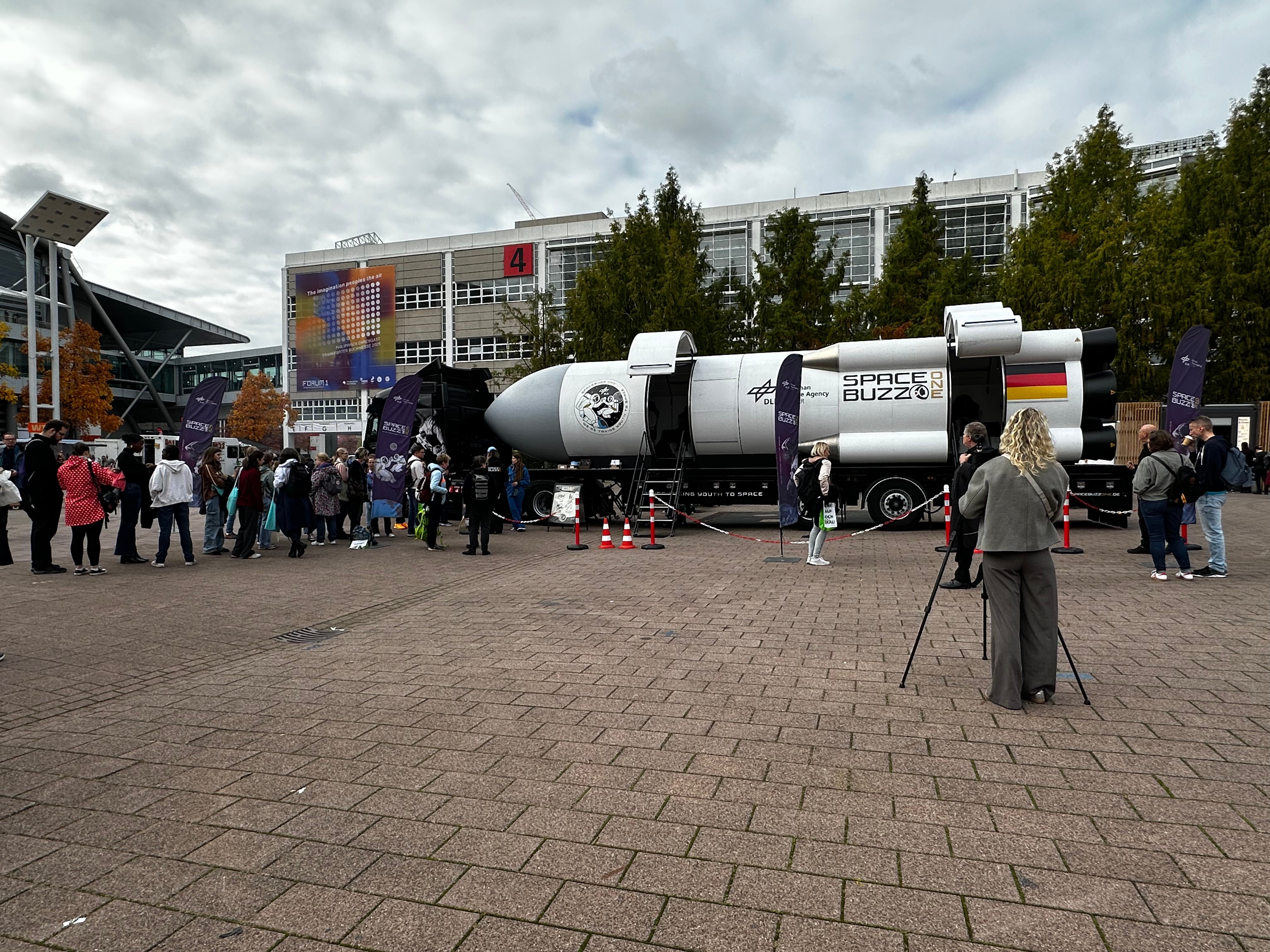 Menschen stehen in einer Warteschlange vor einem mobilen Raumfahrtsimulator namens 'Space Buzz' auf der Frankfurter Buchmesse.