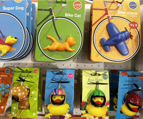 Eine Reihe von Fahrradzubehör aus Kunststoff in Form von Tieren, darunter ein Hund, eine Katze, ein Flugzeug und verschiedene Enten, die zum Verkauf auf Karten präsentiert werden.