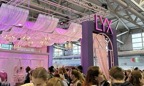 Stand von Lyx auf der Frankfurter Buchmesse, dekoriert mit rosa Draperien und Kronleuchtern, umgeben von Besuchern.