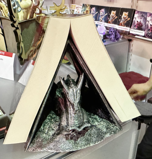 Eine kreative Buchdisplay-Anordnung zeigt zwei aufgeschlagene Bücher, die ein Zelt bilden und eine Skulptur eines Drachen im Inneren präsentieren.