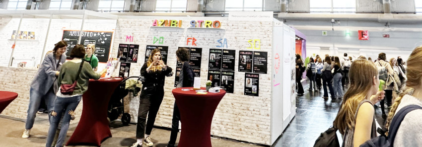 Blick auf den Azu-Bistro Stand auf der Frankfurter Buchmesse, mit Besuchern und Informationsplakaten in einer beleuchteten Halle.