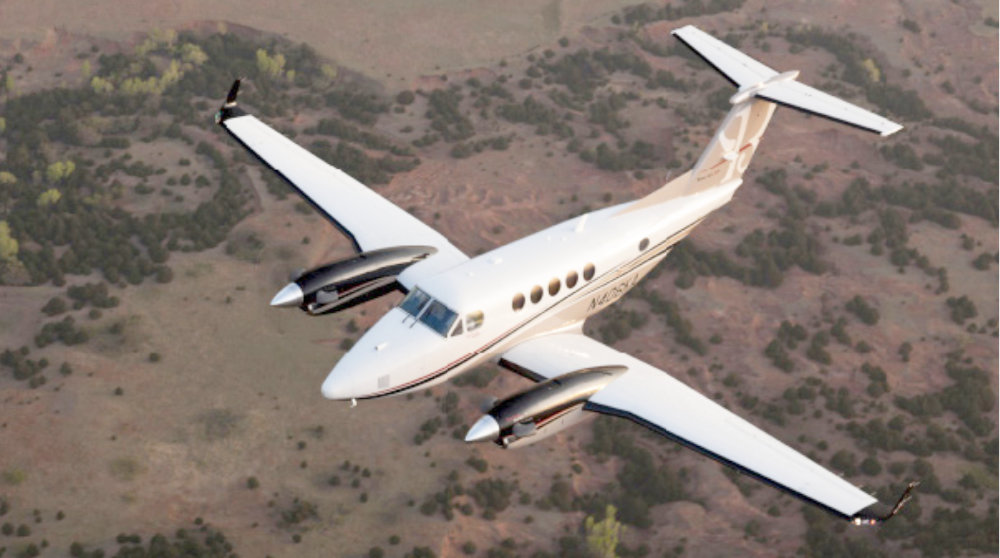 Die Beechcraft King Air 200 fliegt über eine bewaldete Landschaft.